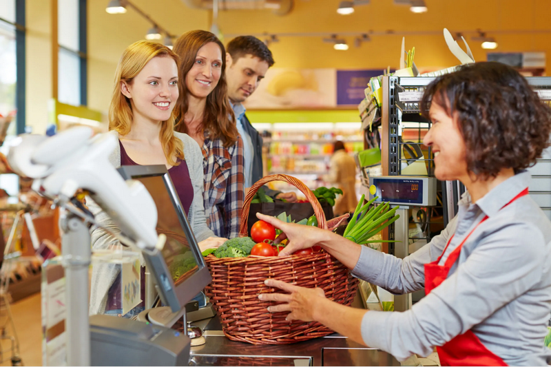 A cashier helps three customers with groceries at a supermarket checkout.